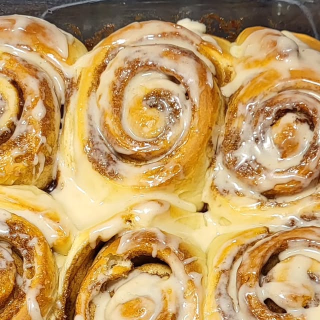 A pan of cinnamon buns flooded with cream cheese icing